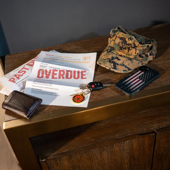 Pile of mail/overdue bills beside a wallet, phone, keys, cover